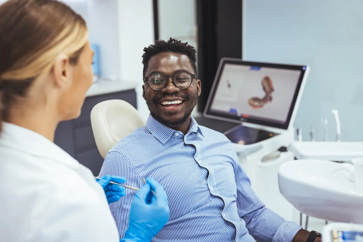Smiling african guy in dentist chair looking with trust at his d