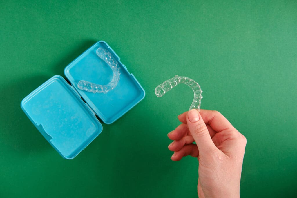Girl holding a plastic mouth guard in her hand, on a green backg
